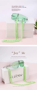 Detail of light green chunky chain sunglasses on a minimalist white display box