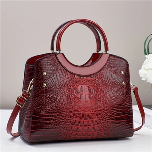 Detail of burgundy crocodile-embossed tote bag with shiny finish and gold rivets