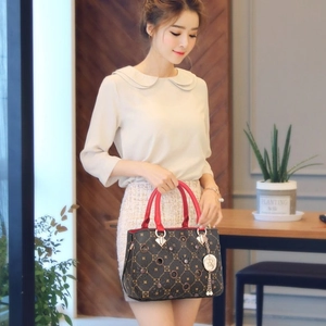 Fashionable brown checkered handbag with red handles and gold charm shown on a table
