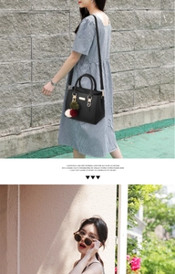 Detail view of a black top-handle bag with a tricolor faux fur pompom and metal logo plate