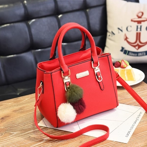 Red lychee grain shoulder bag with plush pompom on wooden table in tea time setting