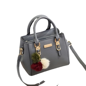 Grey pebbled leather handbag with gold hardware and colorful pom-pom charm
