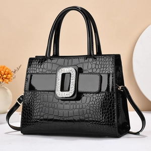 Black crocodile embossed patent leather handbag with sparkling rhinestone buckle on beige background