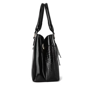 Side view of black patent leather handbag with lizard pattern and gold hardware accents