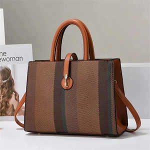 Detail of striped canvas tote with brown leather handles and golden metal buckle clasp