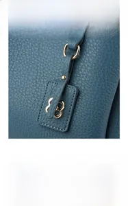 Detail of blue lychee leather bag with metal logo tag and engraved gold snap button