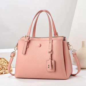 Pink lychee texture handbag with clover charm and adjustable strap on white pedestal
