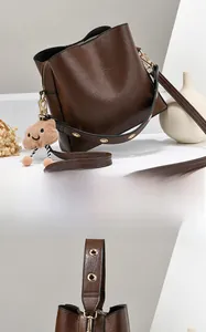 Detail of dark brown leather bucket bag with wide strap and plush bear charm