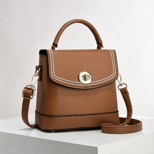 Brown lychee leather bucket bag with top handle and polka dot trim on white pedestal
