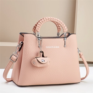 Details einer hellrosa Handtasche mit Litschi-Struktur, Webgriff und modischem Anhänger