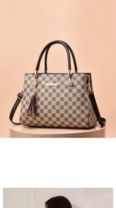 Détail du sac cabas à damier avec logo métallique, anses brunes et pompon rouge décoratif
