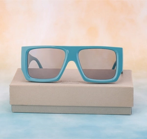 Frontal view of oversized teal square sunglasses on a sustainable paper box base