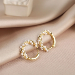 Gros plan de boucles d'oreilles perles dorées torsadées sur un fond de soie élégant