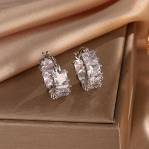 Macro shot of silver-colored hoop earrings with square zircon stones on satin background