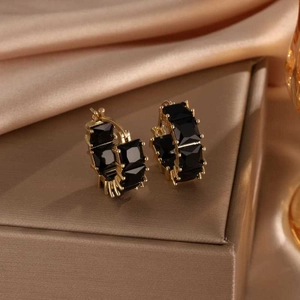 Detail of square black gemstones set in gold-plated hoop earrings on silk background