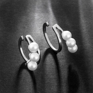 Close-up of minimalist silver ear cuffs with three white pearls on a black textured surface