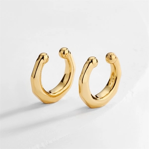 Detail of geometric gold ear cuffs with spherical ends on white minimalist stone surface