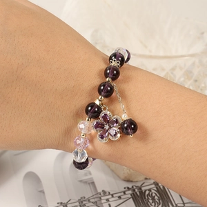 Macro detail of purple crystal beaded bracelet with five-petal floral pendant on wrist