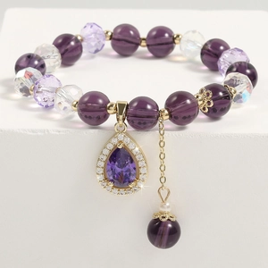 Macro detail of purple crystal bead bracelet with gold teardrop pendant and stones