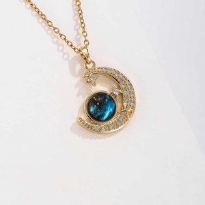 Macro shot of gold crescent moon pendant with blue starry sphere and pave zircon stones