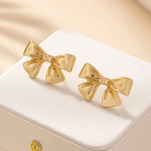 Boucles d'oreilles nœud dorées avec finition polie sur une boîte à bijoux minimaliste
