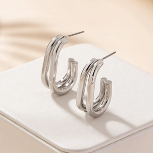 Macro view of silver C-shaped double-line earrings on a textured jewelry box with soft shadows