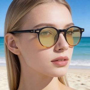 Close-up of dual-tone round sunglasses with amber lenses on model at the beach