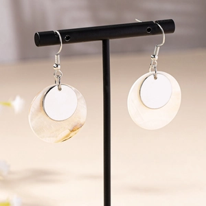 Fashionable shell hoop earrings with silver metal disc on a black display stand