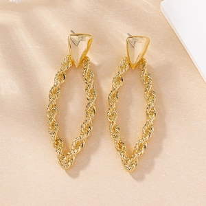 Close-up of golden twist rope oval earrings with geometric studs on beige background