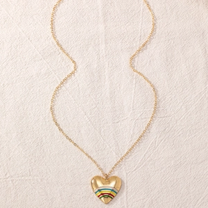 Detail einer goldenen Herz-Halskette mit buntem Regenbogen-Emaille auf beigem Leinenstoff