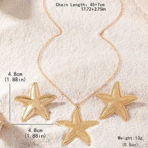 Golden starfish jewelry set with necklace and earrings on white beach sand backdrop