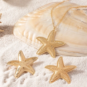 Elegant gold starfish pendant necklace and earrings set displayed on white beach sand