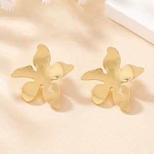 Close-up of golden five-petal flower stud earrings with matte metal texture on stone