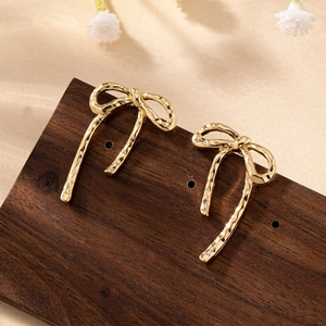 Detailed close-up of golden bow earrings with textured hammered finish and long tassels