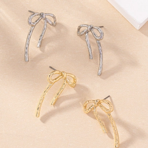 Detailed close-up of gold and silver bow stud earrings with textured metallic finish