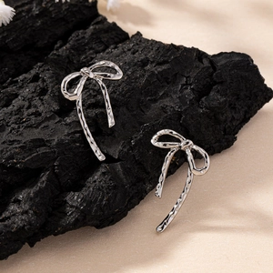 Silver bow stud earrings with hammered texture displayed on a black charcoal block