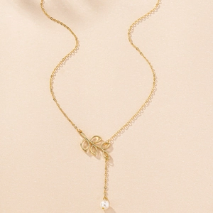 Macro detail of gold necklace featuring hollow olive leaf pendant with white pearl drop