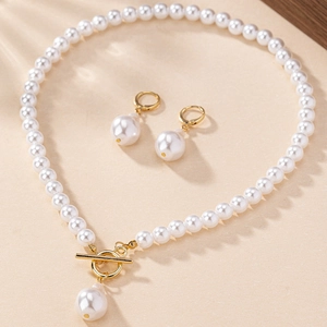 Elegant gold pearl necklace and earrings set with toggle clasp on a textured surface
