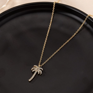 Gold palm tree pendant necklace with white crystals on a luxury black display