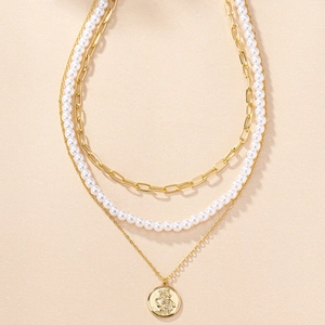 Close-up of triple-layered gold necklace with pearl strand and religious coin pendant