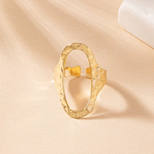 Detail of gold open ring with hammered texture and oval cutout on beige background