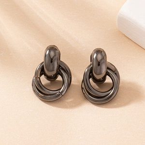 Détail de boucles d'oreilles créoles multicouches imbriquées en métal noir sur fond beige