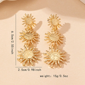 Elegant gold-tone triple sunburst dangle earrings with textured finish on beige surface