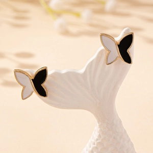 Elegant black and white enamel butterfly stud earrings with gold trim on jewelry stand
