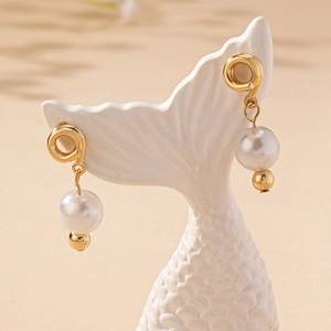 Elegant gold knot earrings with large pearl drop hanging on a ceramic display stand