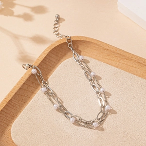 Detail of double-layer silver chain bracelet with white pearls on a minimalist tray