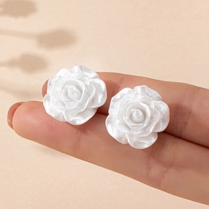 Elegant white rose stud earrings with pearlescent finish shown on a finger for size