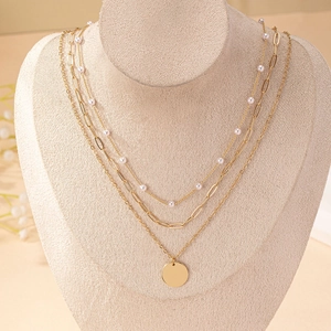 Three-layer gold necklace featuring pearls, paperclip chain, and a round disc pendant