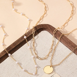 Three-layer gold layered necklace set with pearls and circular pendant on warm backdrop