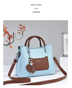 Detail of blue textured handbag with brown straps and heart-shaped metal pendant
